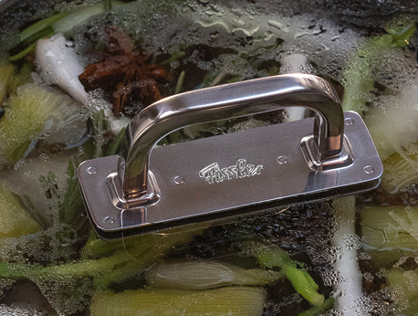 Nahaufnahme eines Fissler-Topfdeckels aus rostfreiem Stahl mit Kondenswasserbildung, wobei grüne Zwiebeln und Sternanis im Inneren des Dampfkochtopfes zu sehen sind.