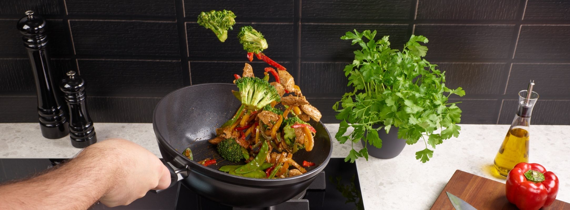 Ein Koch brät fachmännisch Gemüse und Fleisch in einem Fissler-Wok und präsentiert dabei hochwertiges deutsches Kochgeschirr und frische Zutaten auf der Theke.