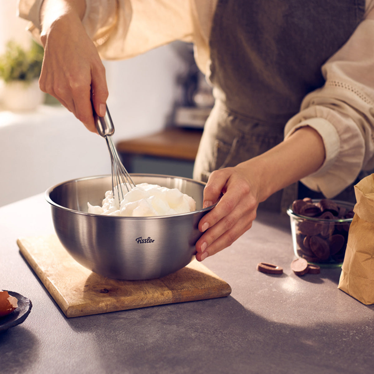 Eine Person rührt Zutaten in einer Fissler Essential® Schüssel 20cm; Schokolade und eine Papiertüte liegen auf der hochwertigen Küchentheke.
