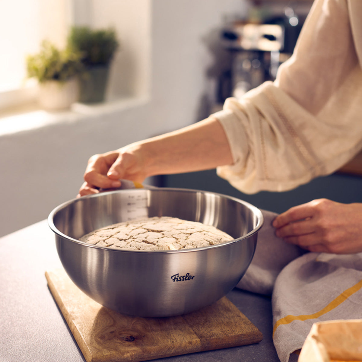 Eine Person präsentiert den aufgegangenen Teig in einer Fissler Essential® Schüssel 24cm, die deutsche Präzision und zeitloses Küchendesign verkörpert.