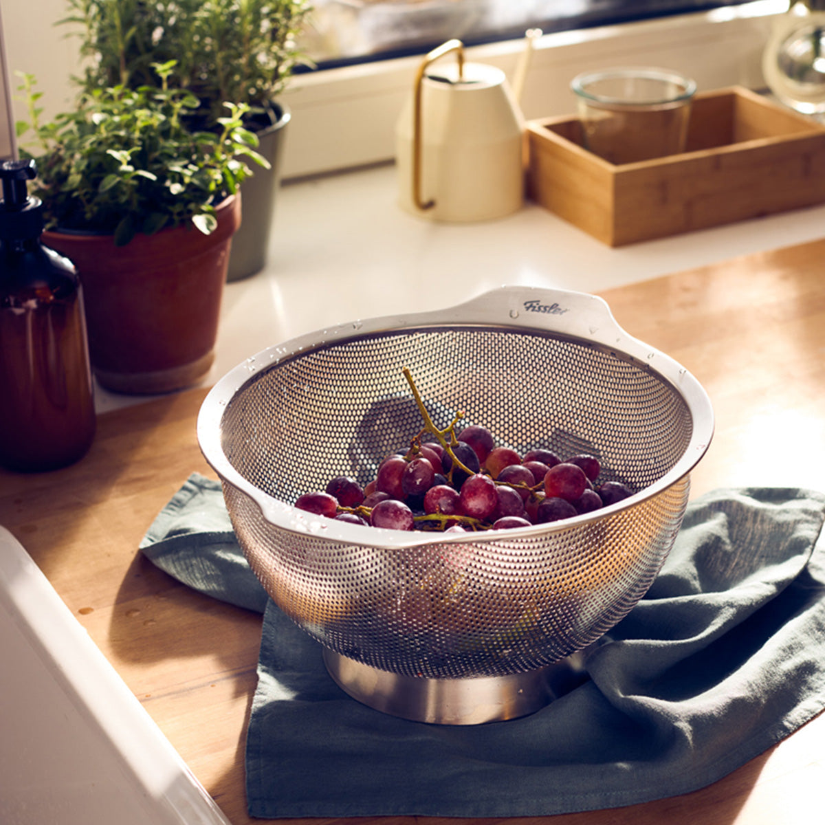 The Fissler Essential® 24cm sieve, made in Germany, holds red grapes on the kitchen counter and shows timeless Fissler quality.