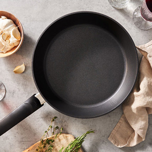 Fissler Levital®+ Comfort Frying Pan on a grey countertop with beige cloth, garlic, herbs and glasses - timeless precision cookware made in Germany.