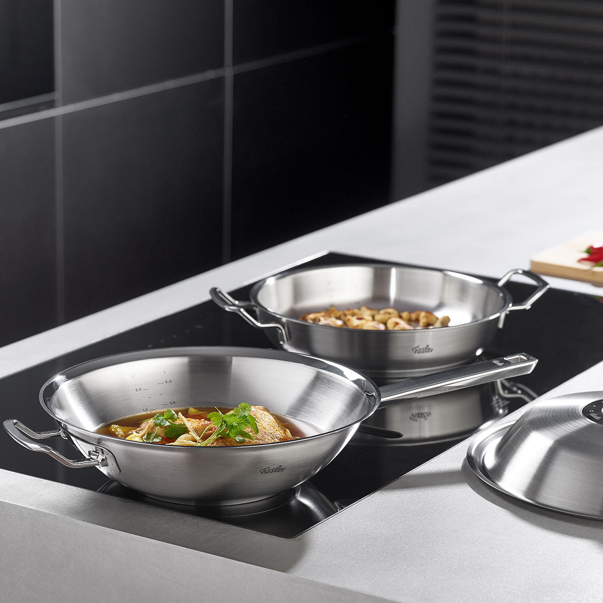 Two Fissler stainless steel pots on the stove - one with vegetable stew, one with pasta; the lid of the Fissler pot lies on the counter next to them.