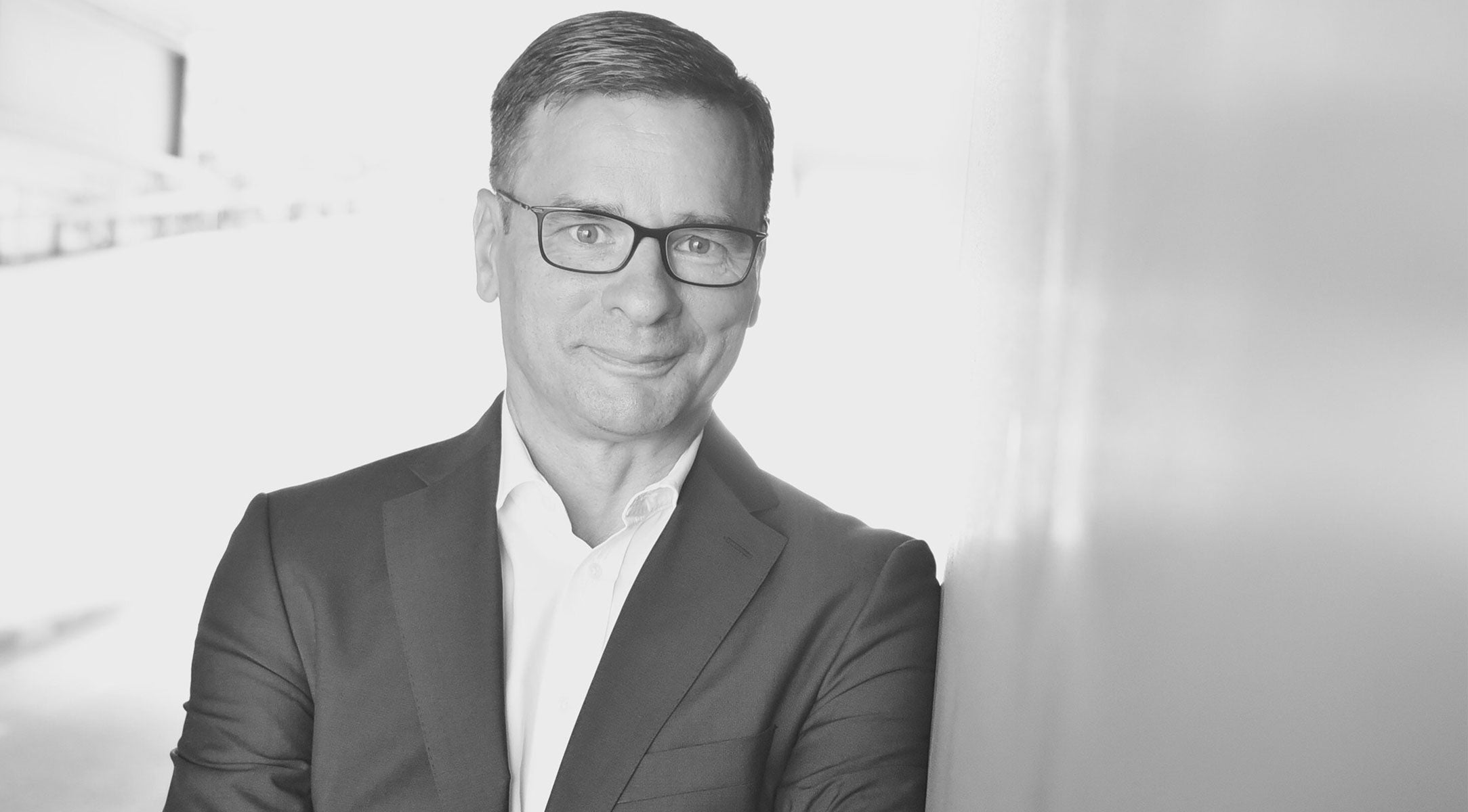Schwarz-Weiß-Foto eines Mannes im Anzug und mit Brille, der mit verschränkten Armen lächelt und den Geist von Fisslers zeitlosem deutschen Design beschwört.
