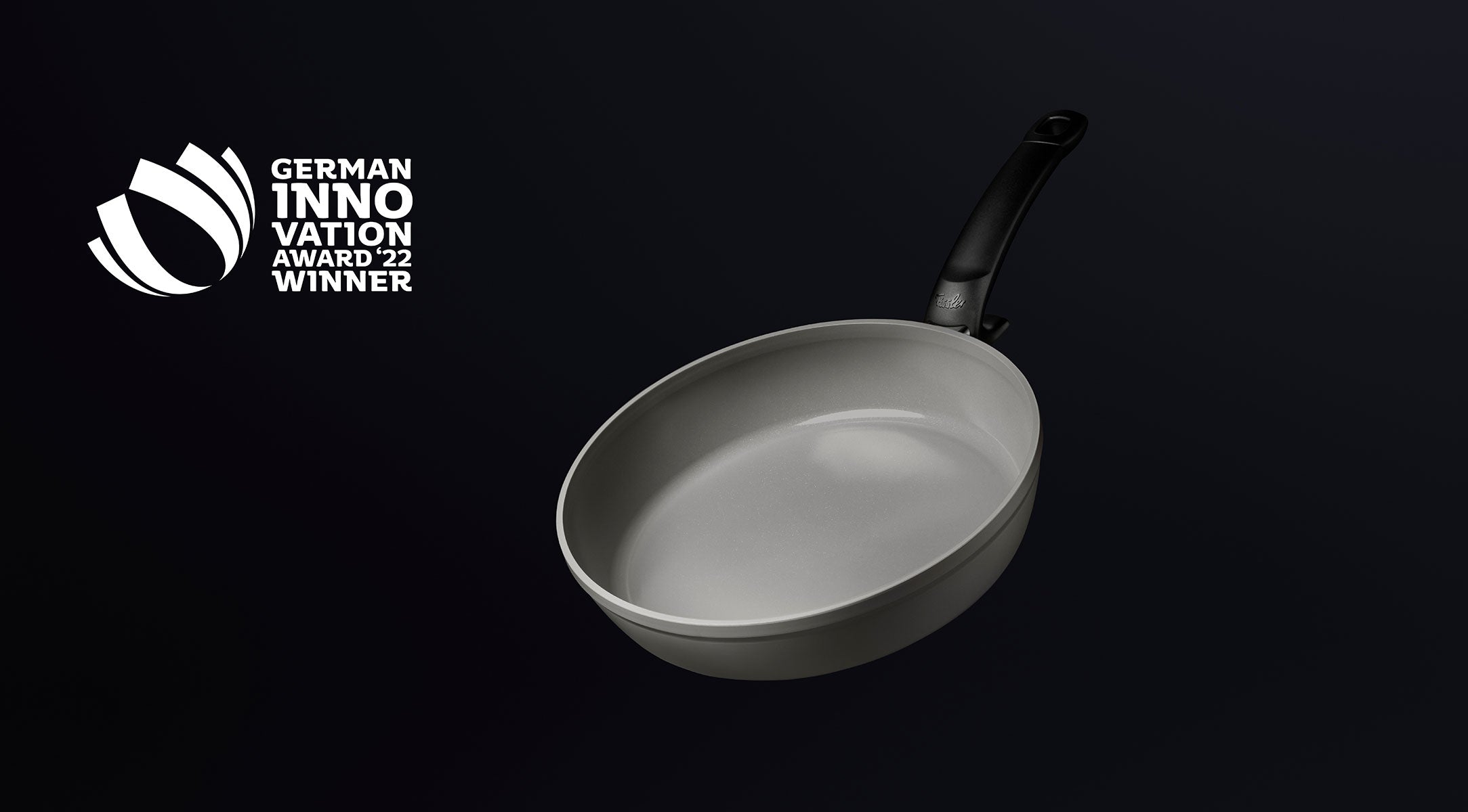 Graue Fissler Bratpfanne mit schwarzem Griff auf dunklem Hintergrund; links das Logo des German Innovation Award 22 Winner.