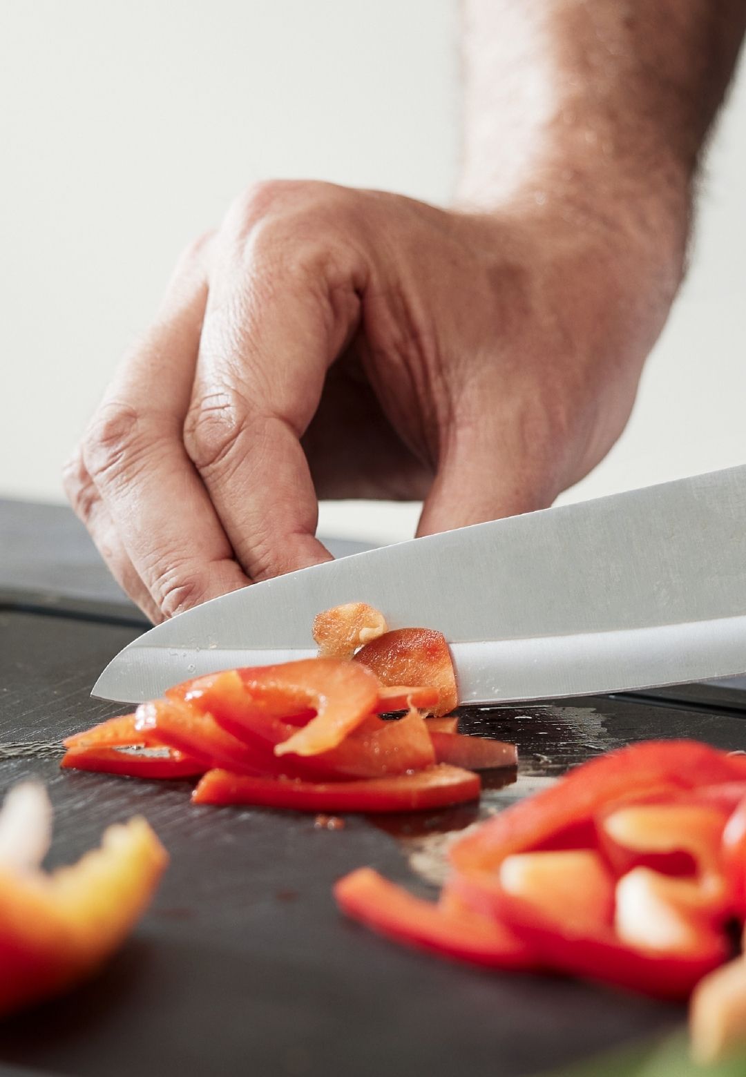Nahaufnahme einer Hand, die eine rote Paprika mit einem Fissler-Kochmesser auf einem glatten schwarzen Schneidebrett präzise schneidet.