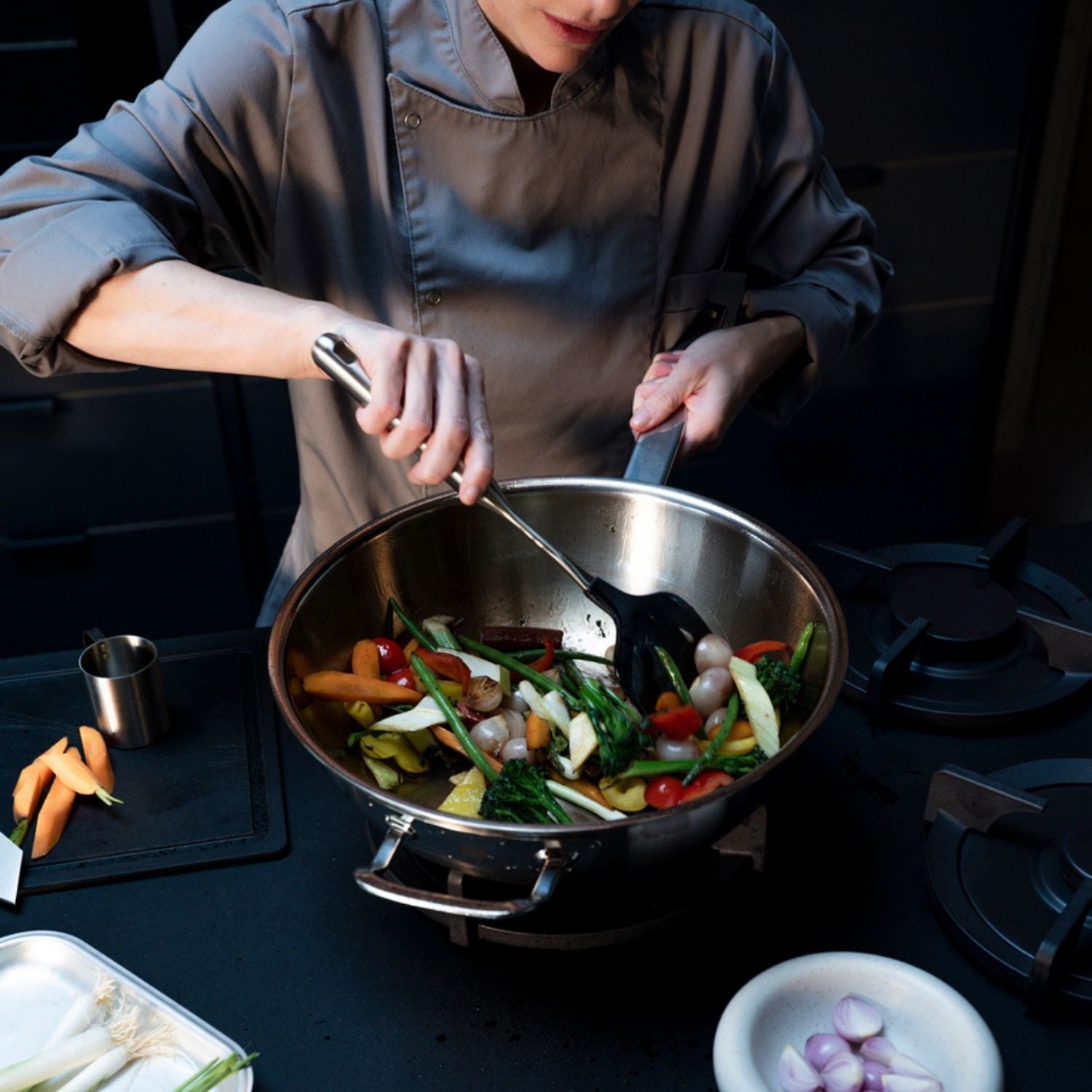 Ein Küchenchef bereitet in einem hochwertigen Fissler-Wok mit frischem Gemüse und hochwertigem Kochgeschirr auf der Küchentheke ein lebhaftes Wokgericht zu.