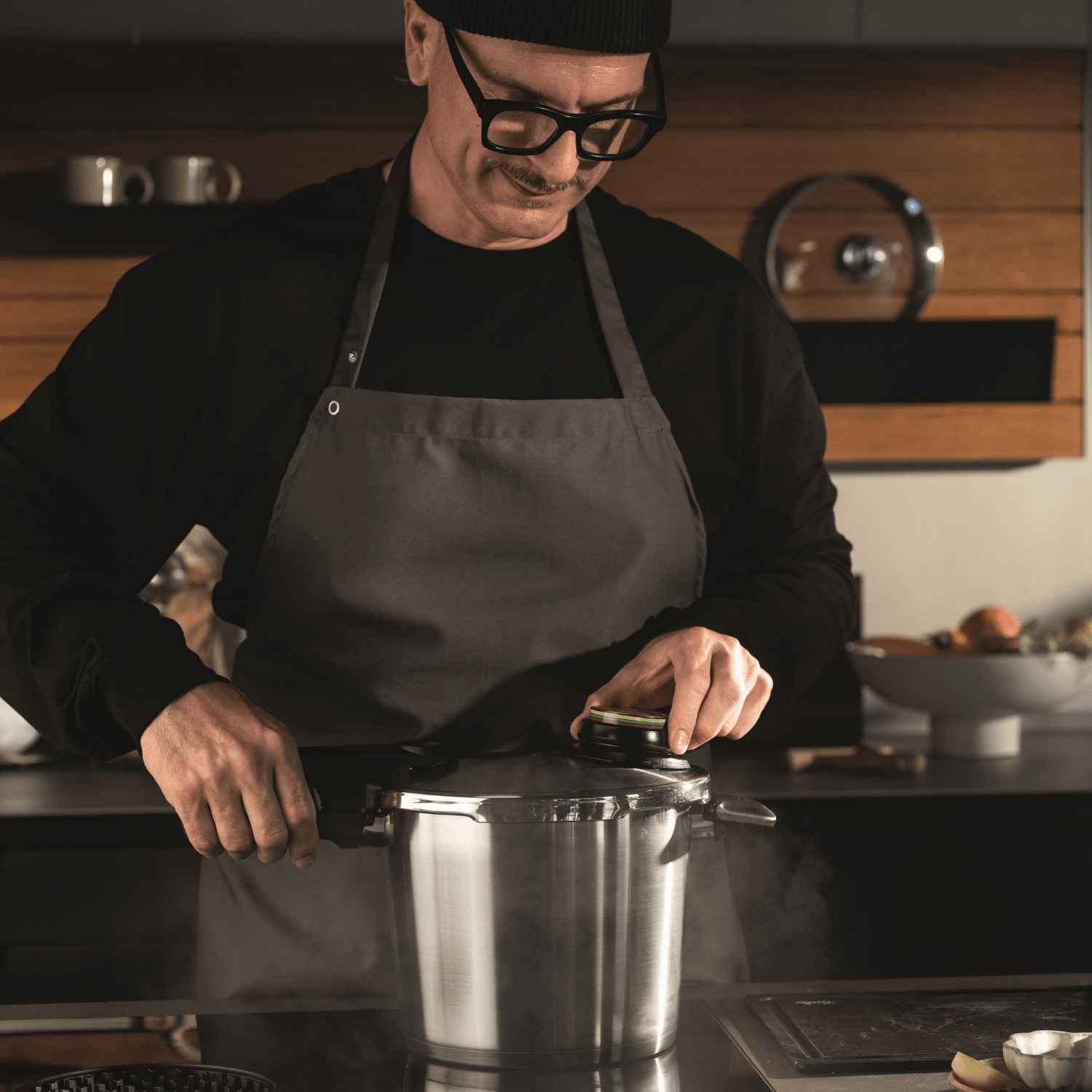 Eine Person in einer modernen Küche öffnet einen dampfenden Fissler Schnellkochtopf aus Edelstahl, der deutsche Präzision und Innovation demonstriert.