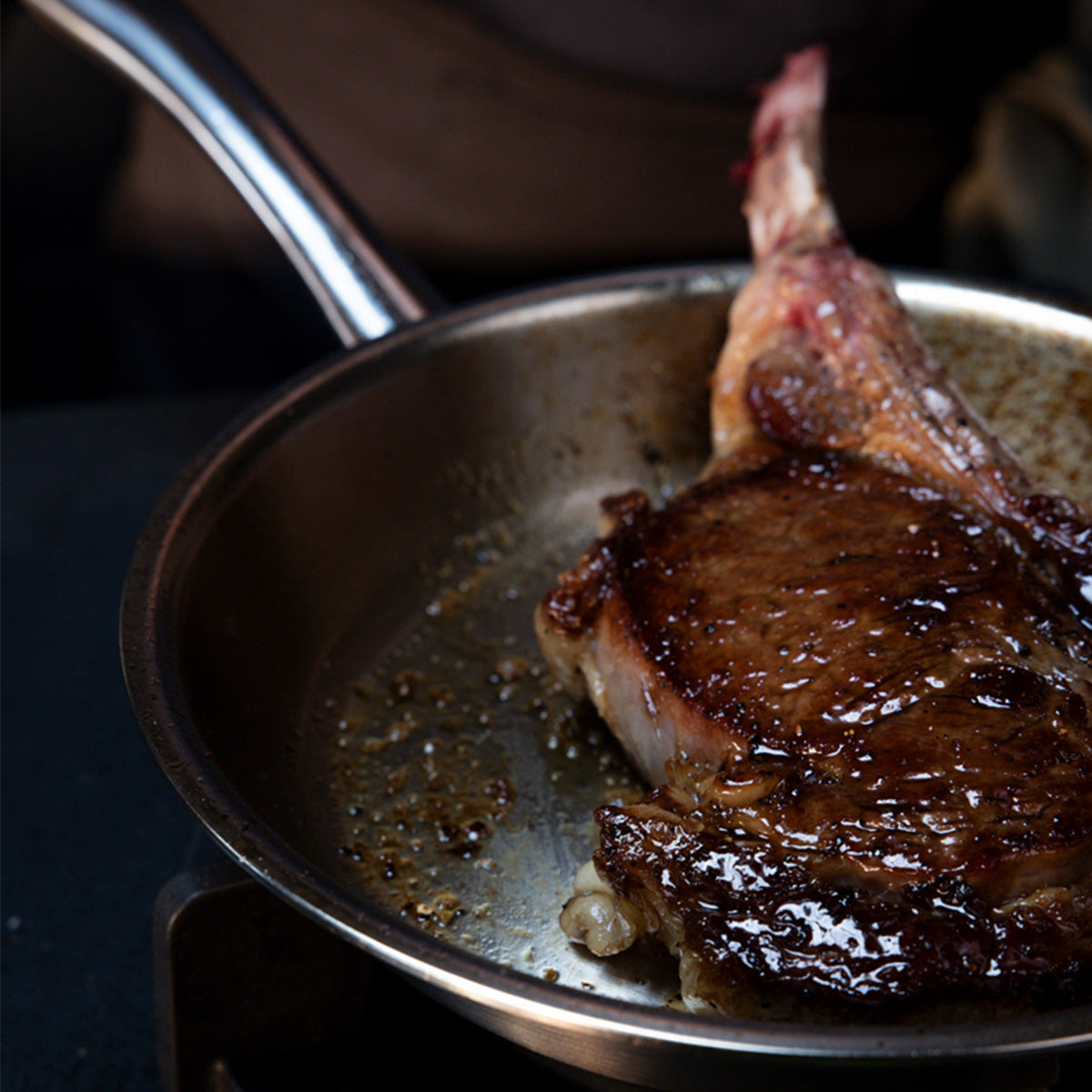 Ein Steak mit Knochen, mit einer kräftigen braunen Kruste und saftigem Fleischinnerem, wird im Fissler M5 Pro-Ply® 3-tlg. Set mit Metalldeckel auf einem induktionsgeeigneten Kochfeld perfekt angebraten. Das Bild unterstreicht die für Fissler charakteristische Präzisionstechnik und das zeitlose deutsche Design und demonstriert die langlebige Leistungsfähigkeit für außergewöhnliche Kochergebnisse.