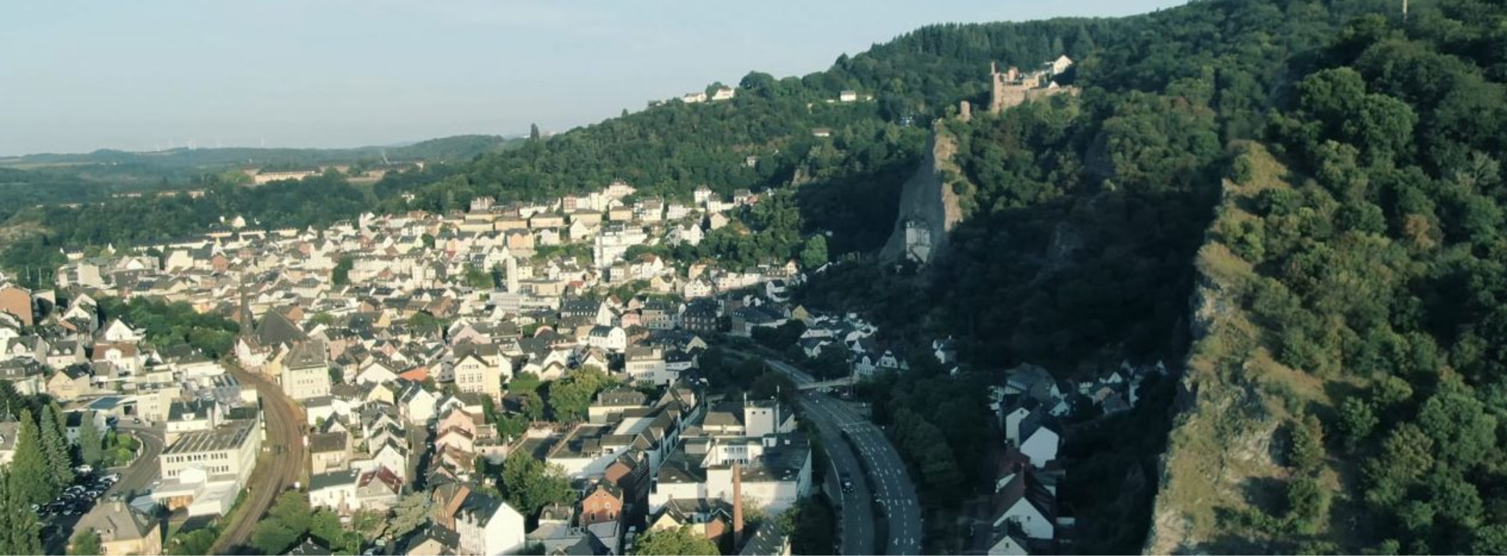 Luftaufnahme einer deutschen Stadt mit üppigen Hügeln und Burgruinen, die Fisslers Erbe von Präzision und zeitlosem Design widerspiegelt.