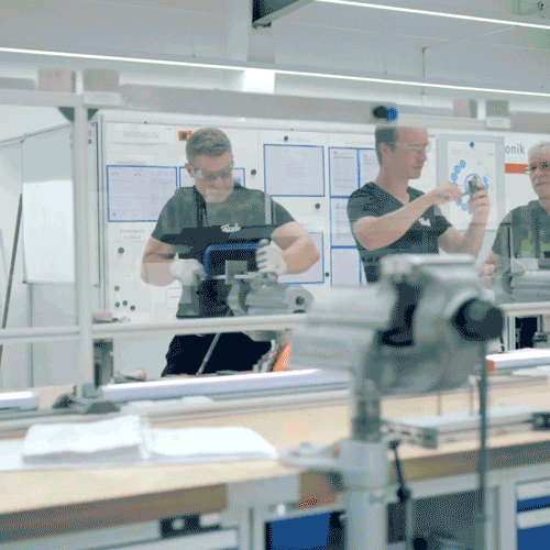 Drei Experten fertigen und prüfen in einer unberührten Fissler-Werkstatt hochwertiges Kochgeschirr aus Edelstahl hinter Glas, das deutsche Präzision widerspiegelt.