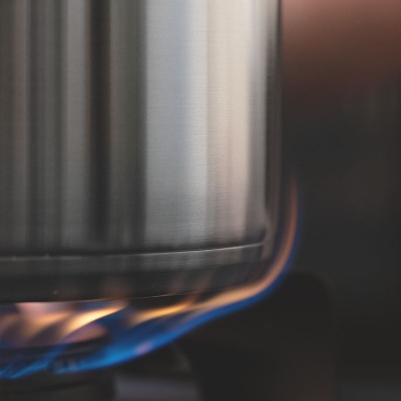 A close-up of a Fissler stainless steel pot, precision-engineered in Germany, sitting on a stove as a blue gas flame evenly heats its durable base—exemplifying timeless design and innovative craftsmanship.