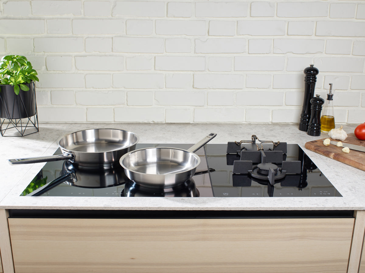 Fissler Original-Profi Collection® Pfannen mit frischen Zutaten auf einer eleganten Herdplatte; deutsche Qualität, zeitloses Design.
