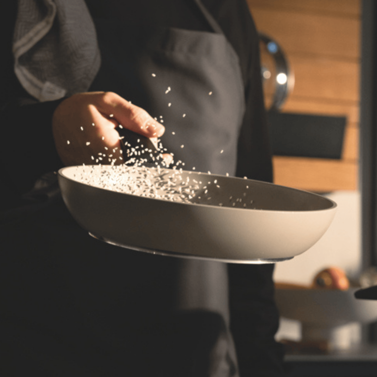 Ein Heimkoch in dunkler Schürze schwenkt Reis in einer hochwertigen Fissler-Pfanne und präsentiert deutsche Qualität und Präzision im warmen Küchenlicht.