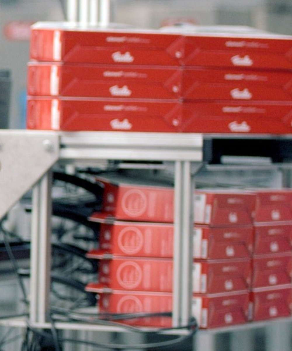 Stapel der ikonischen roten Fissler-Kartons, präzise verpackt auf einem Förderband in unserem deutschen Werk, bereit für die Lieferung von Premium-Kochgeschirr.