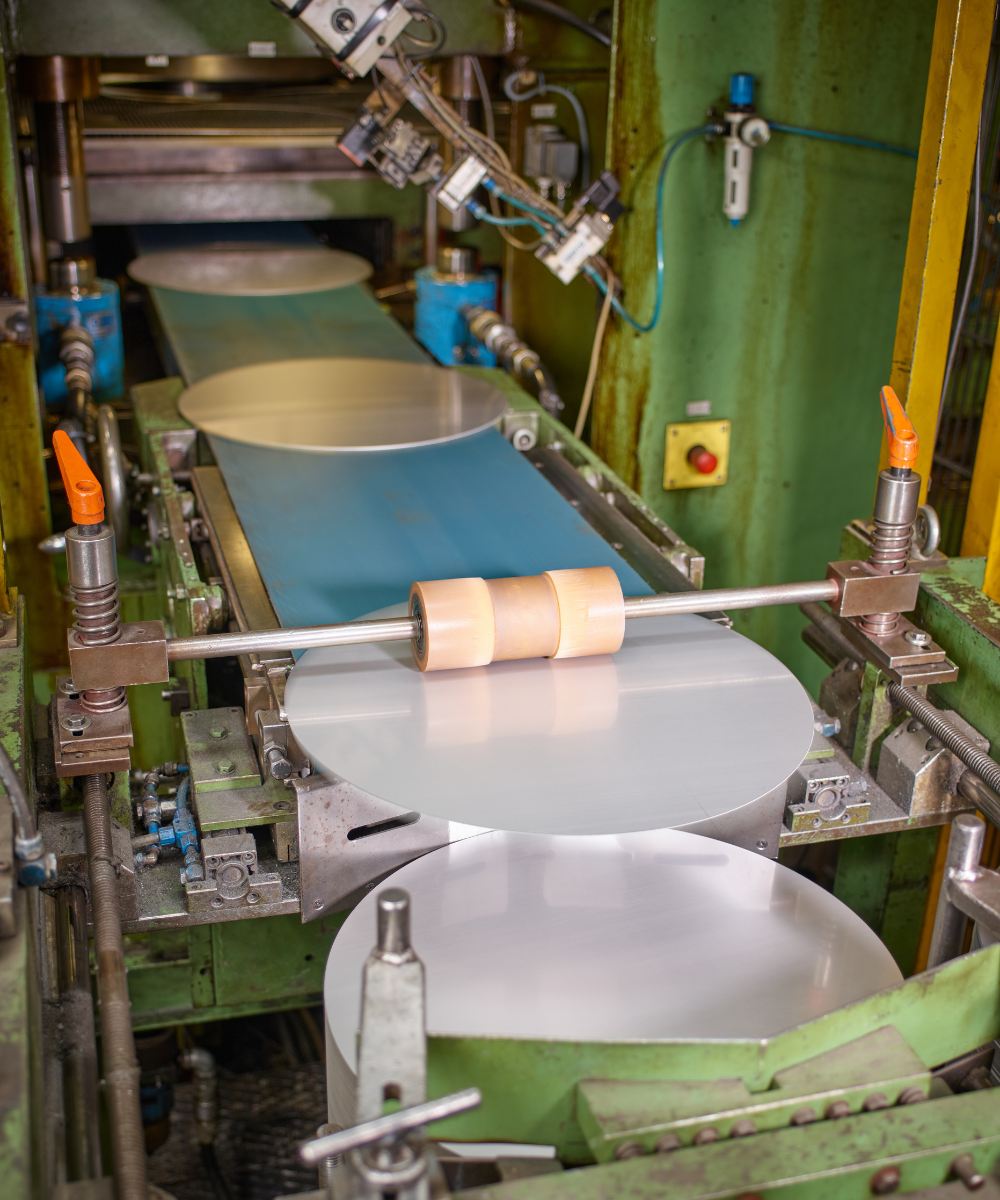 Eine Nahaufnahme der Maschinen in der Fissler-Fabrik, die hochwertiges Kochgeschirr formen, mit Präzisionswalzen, die Aluminiumbleche auf der Fertigungsstraße führen.
