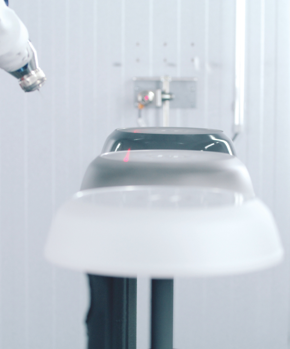 In der makellosen, hellgrauen Fissler-Fertigungsstätte trägt ein Roboterarm präzise eine Lackierung auf hochwertiges Edelstahl-Kochgeschirr auf.