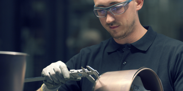 Ein Techniker in Schutzkleidung misst in der deutschen Werkstatt von Fissler ein Kochgeschirrteil aus Edelstahl mit einem Messschieber genau aus.