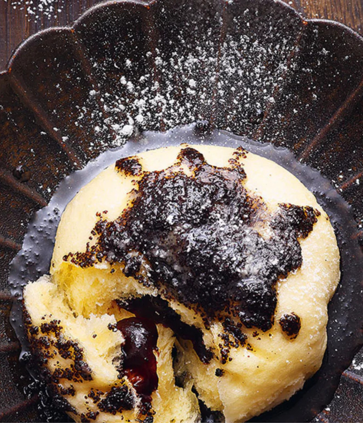 A fluffy, golden pastry dusted with powdered sugar sits on a dark, baked plate - precisely served, inspired by Fissler tradition.