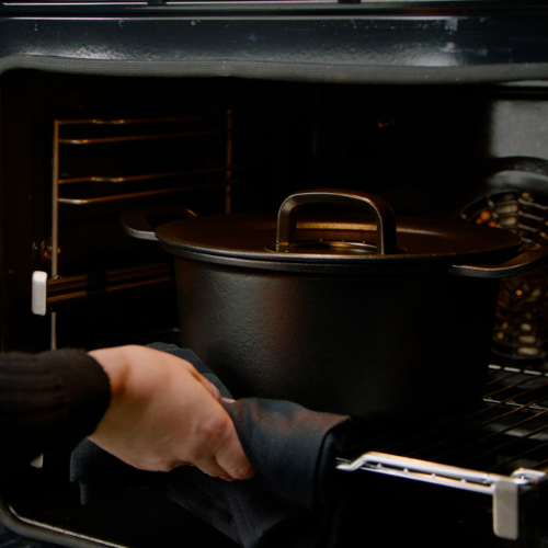 A person places a Fissler cast iron Dutch oven with lid on an oven rack, using a pot holder for safety - timeless German design.