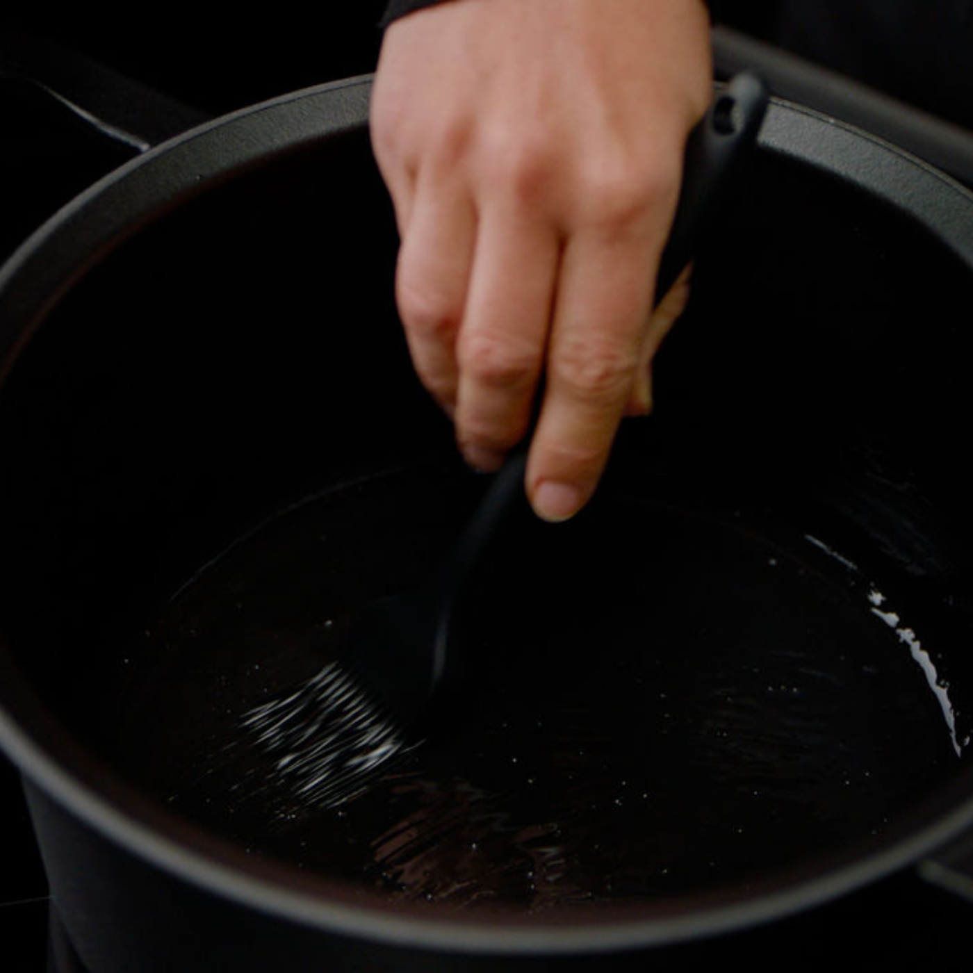 A hand uses a Fissler brush to apply oil in a high-quality black Fissler pot, preparing the durable cookware for precision cooking.