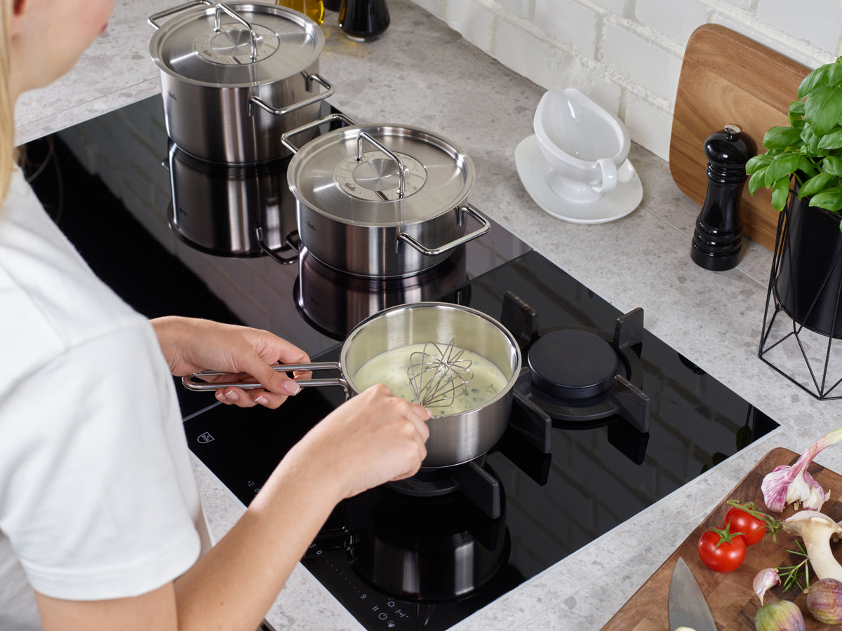 A creamy mixture is whipped in the Fissler Pure Collection 16 cm saucepan with two Fissler stainless steel pots on a modern stove.