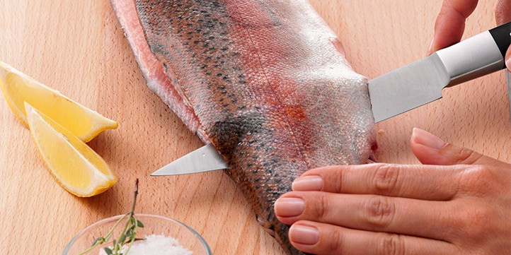 A precise knife cuts the fish fillet on a wooden board, with lemon slices and salt next to it - proof of Fissler's kitchen innovation.
