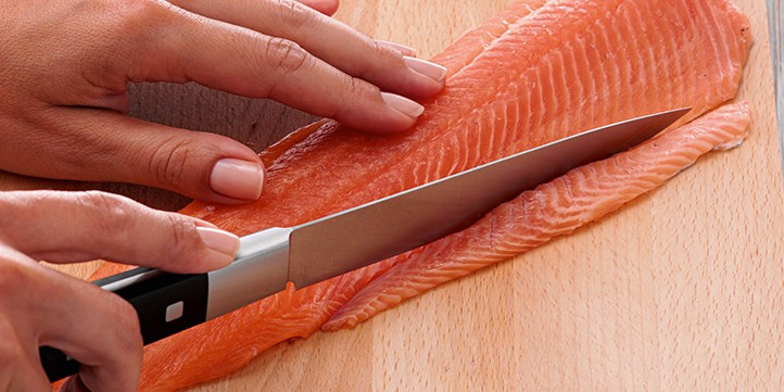 A person expertly slices fresh salmon on a wooden board with a Fissler precision knife - timeless German quality in action.