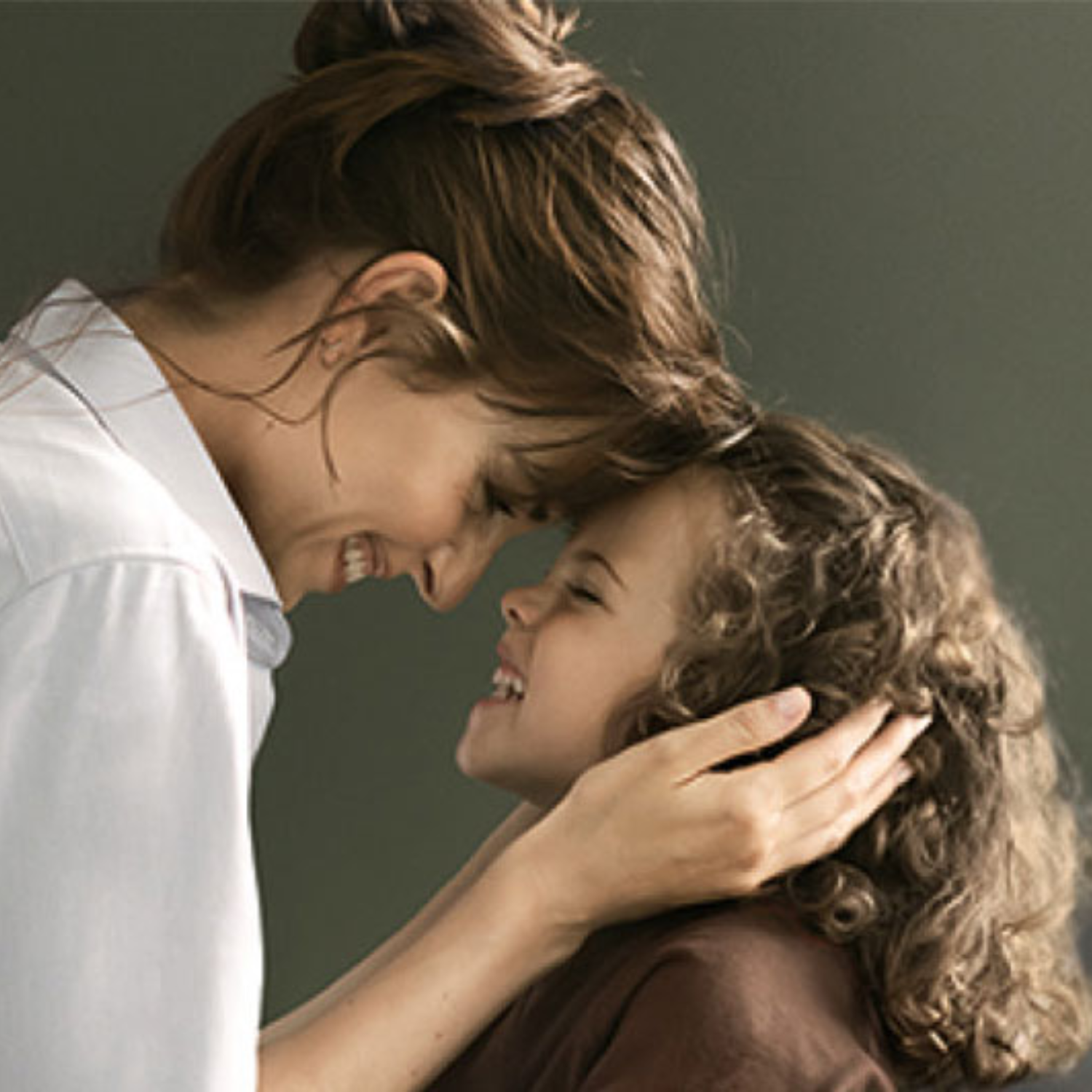 A woman and a girl with curly hair smile in a kitchen featuring elegant Fissler stainless steel cookware, enjoying the moment.