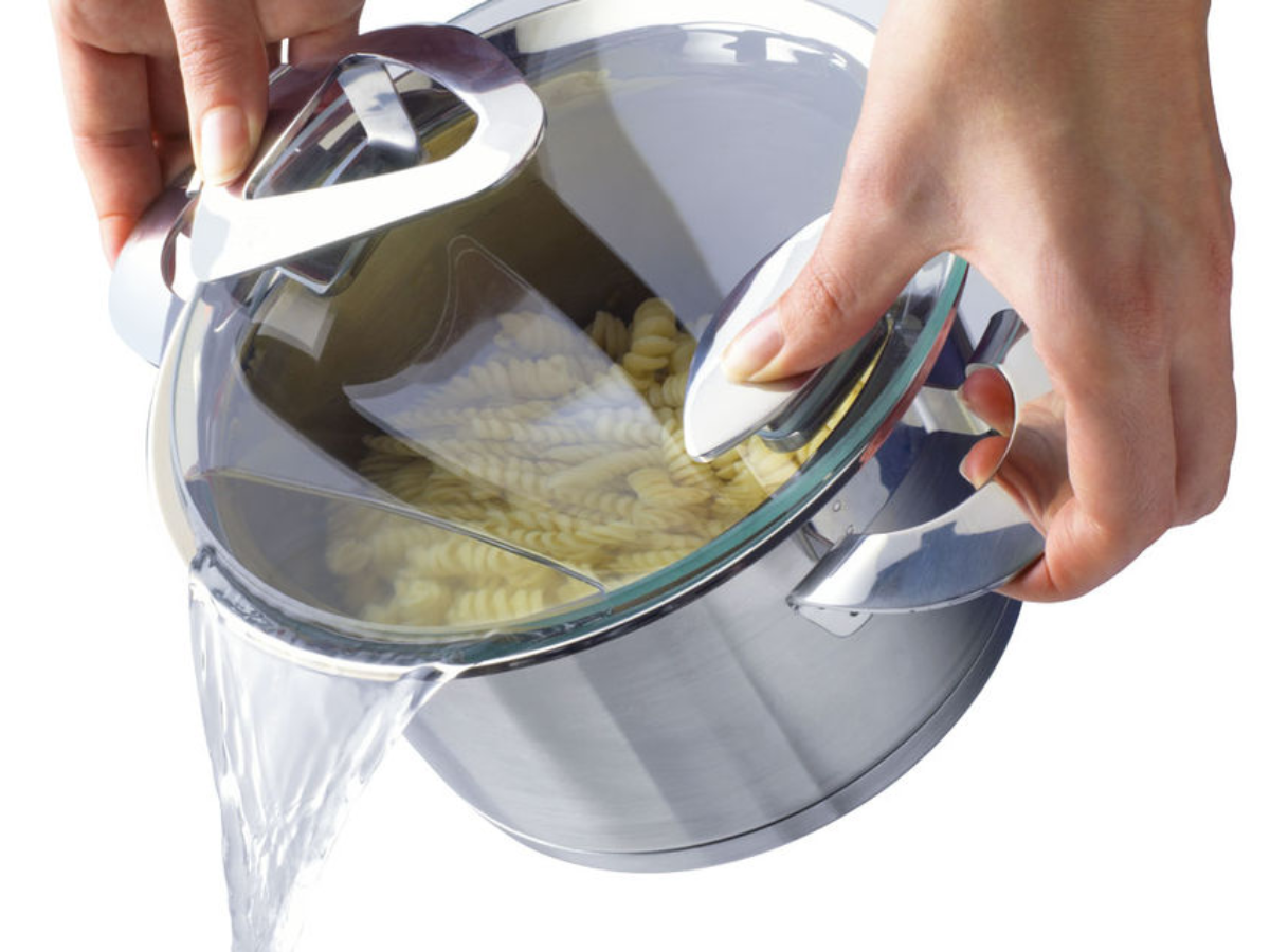 A person purees pasta in a Fissler stainless steel pot with an integrated colander lid, showcasing German engineering and design.