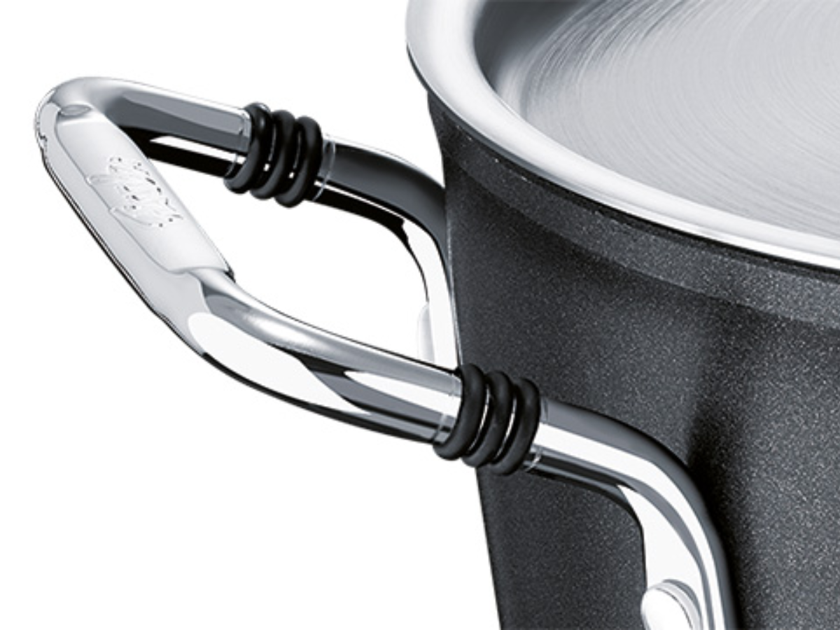 Close-up of a black Fissler pot with a precision-crafted metal handle, two handle rings, and the characteristic stainless steel lid.