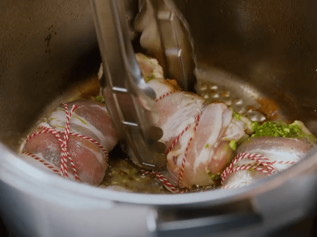 Bacon-wrapped chicken breasts are seared in a Fissler stainless steel pot held with tongs - precision, quality "Made in Germany".