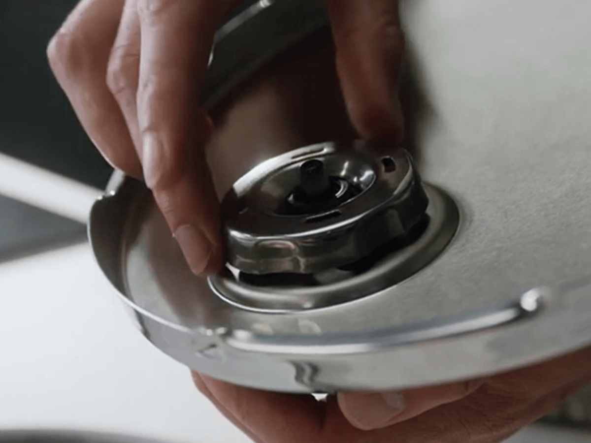 Close-up of a hand precisely adjusting the safety valve on a Fissler stainless steel pressure cooker lid, demonstrating German quality.