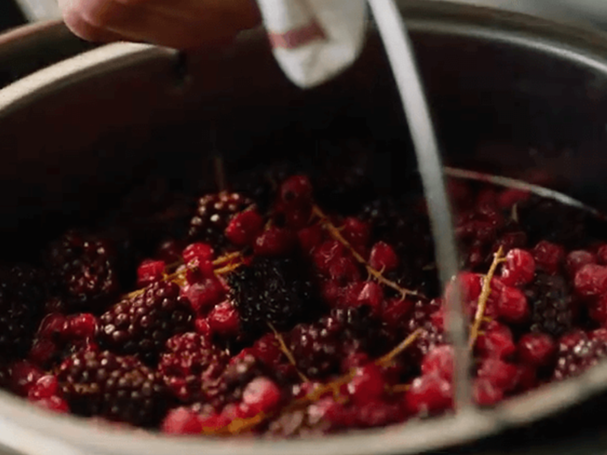 A Fissler stainless steel pot filled with fresh blackberries and red currants, as a hand carefully prepares the berries with a cloth.
