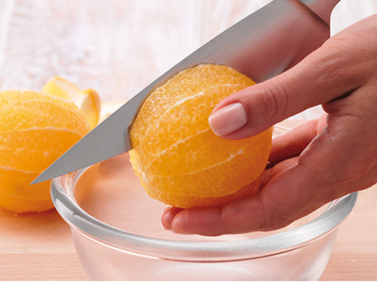 A person precisely cuts a peeled orange with a high-quality Fissler knife over a glass bowl, with another orange next to it.