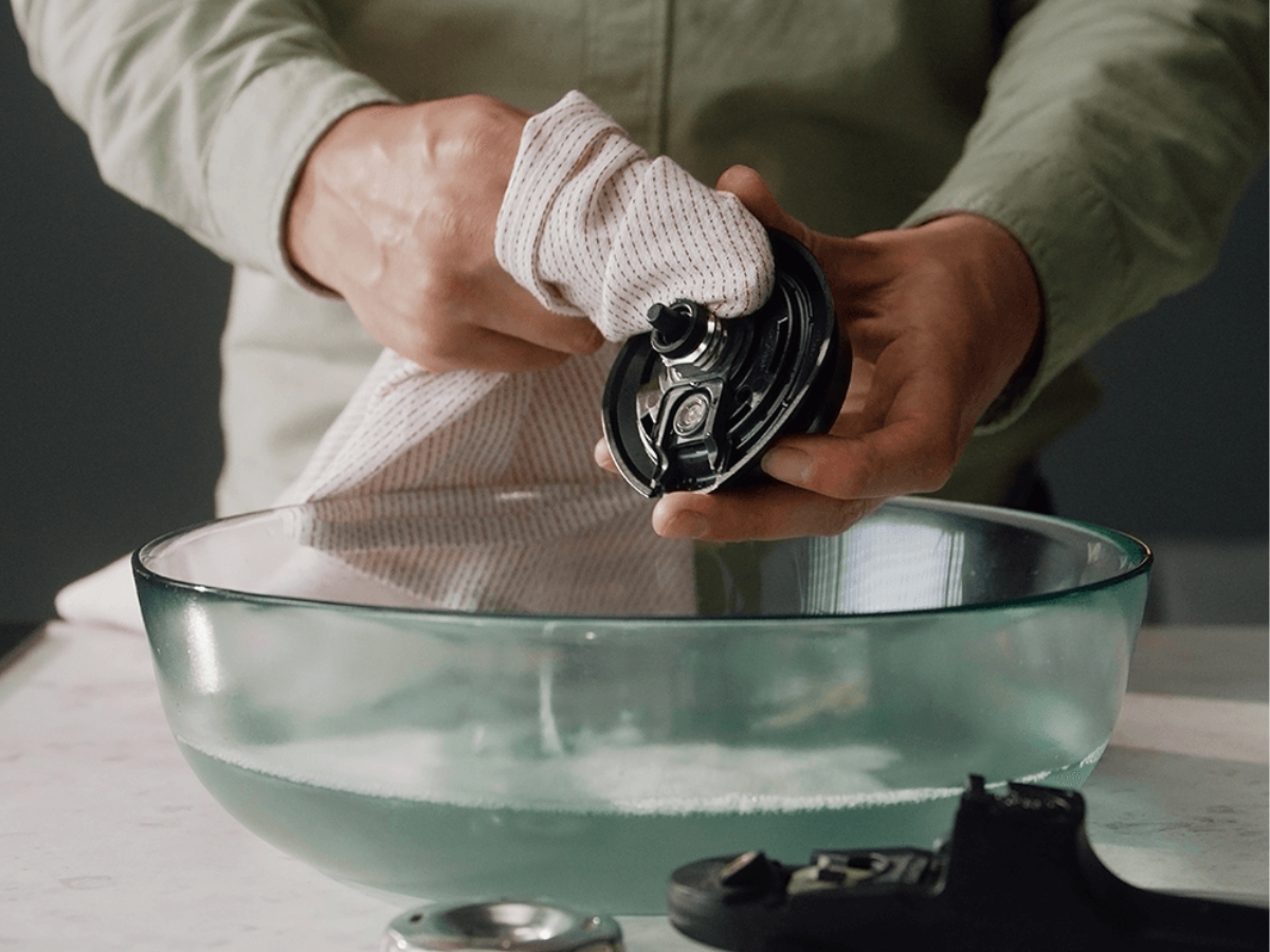 Eine Person trocknet ein Fissler-Schnellkochtopfteil mit einem Tuch über einer Glasschüssel auf einer weißen Arbeitsplatte ab und verkörpert damit deutsche Präzision.