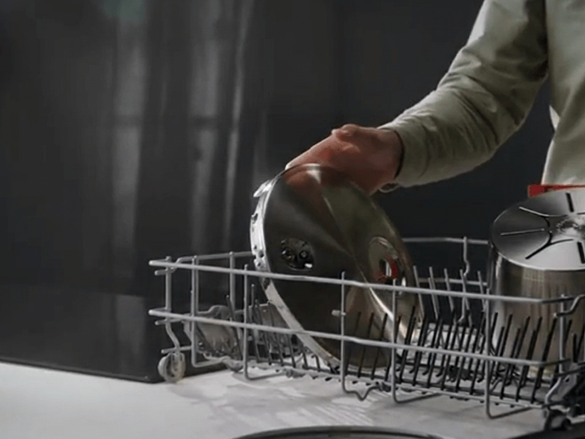 A person loads a Fissler stainless steel pot lid into the bottom rack of a dishwasher, highlighting the brand’s exceptional German craftsmanship and easy-care design.