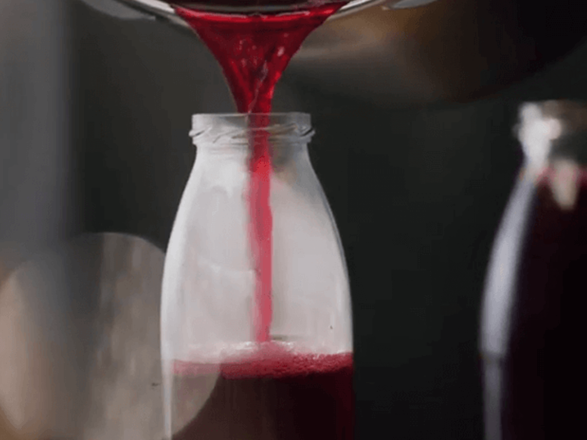 A bright red liquid is poured into a clear Fissler glass bottle. The dark, blurred background emphasizes the high-quality design.