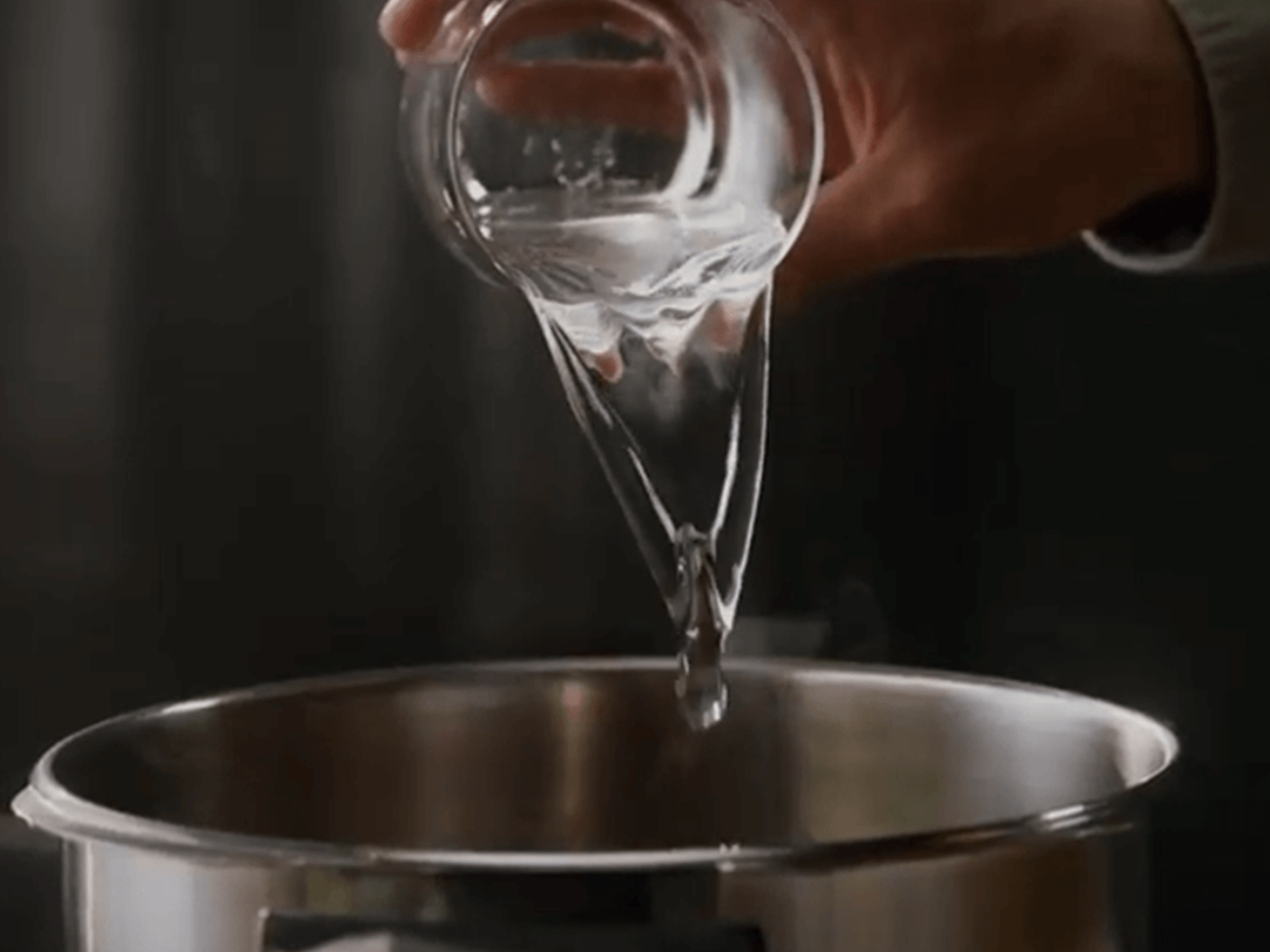 A hand pours water from a glass into a high-quality Fissler stainless steel pot, showcasing German engineering and timeless design.