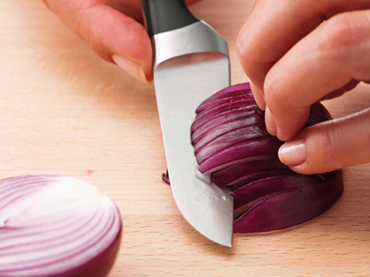 Eine Person schneidet mit einem Fissler-Messer fachmännisch eine rote Zwiebel auf einem Holzbrett und demonstriert damit deutsche Präzision und Qualitätshandwerkskunst.