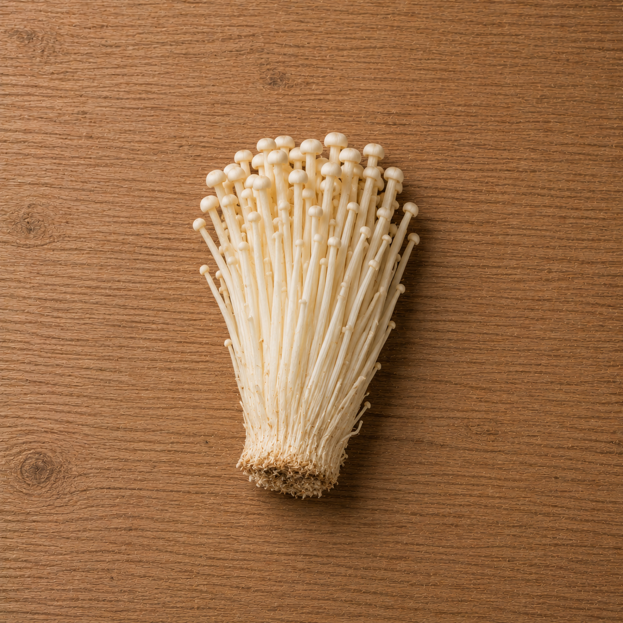 Enoki mushrooms with long, slender white stems and petite caps arranged on a wooden surface, ready for preparation in Fissler’s precision-engineered cookware.