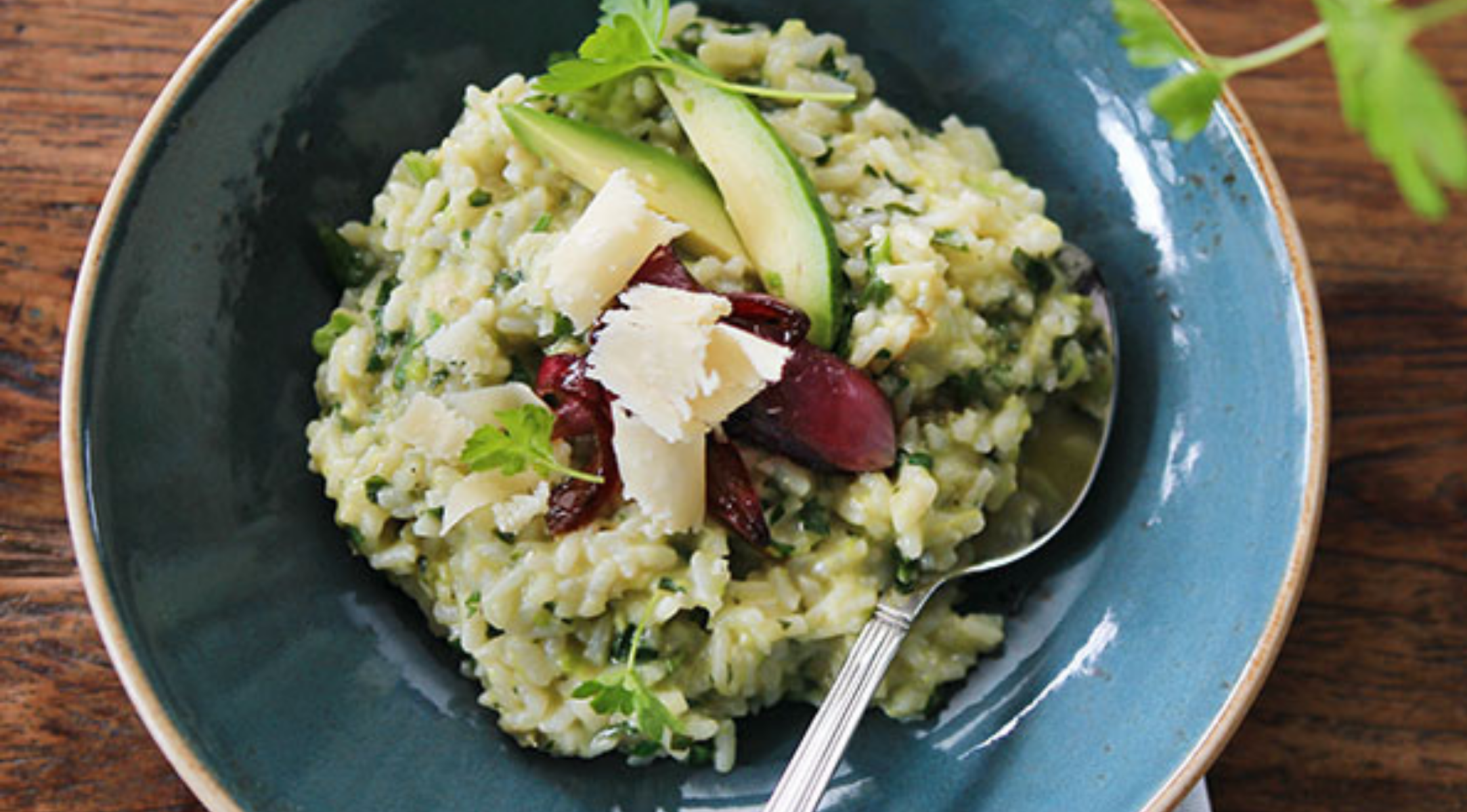 Eine Schüssel cremiges Risotto mit Avocado, Oliven, Käse und Kräutern auf dem Holztisch - zubereitet im Fissler Kochgeschirr für perfekte Ergebnisse.