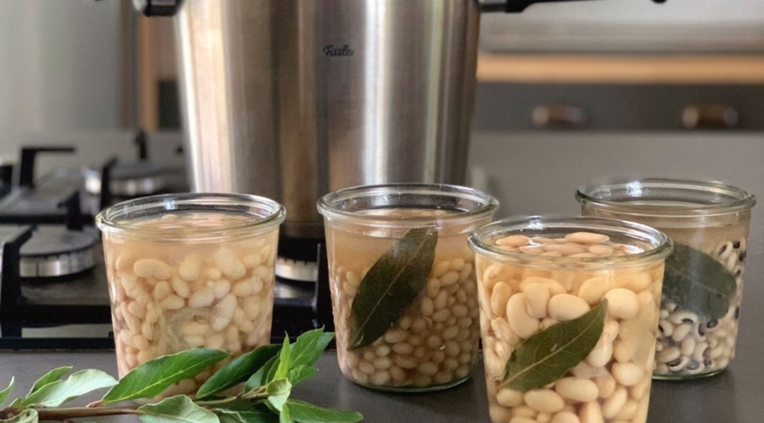 Drei Gläser mit Bohnen und Lorbeerblättern stehen neben einem hochwertigen Fissler-Edelstahl-Schnellkochtopf auf einer modernen Küchenzeile.