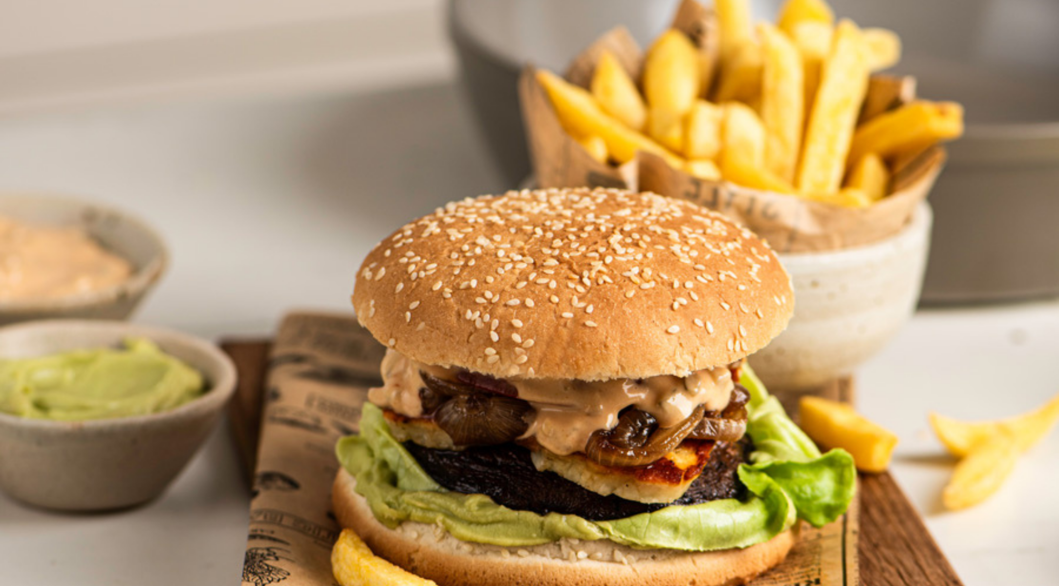 Ein Gourmet-Burger, serviert auf einem Holzbrett, mit Pommes frites und Saucen - perfekt zubereitet mit dem hochwertigen Fissler-Kochgeschirr.