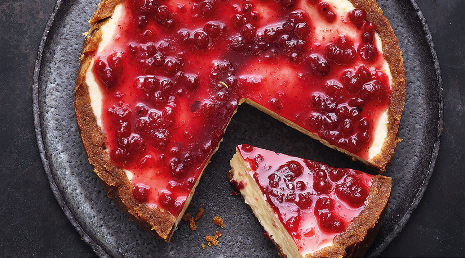 Ein cremiger Käsekuchen mit roter Beerensauce liegt auf einem dunklen Teller - perfekt geschnitten mit dem Präzisionskochgeschirr von Fissler für makellose Ergebnisse.