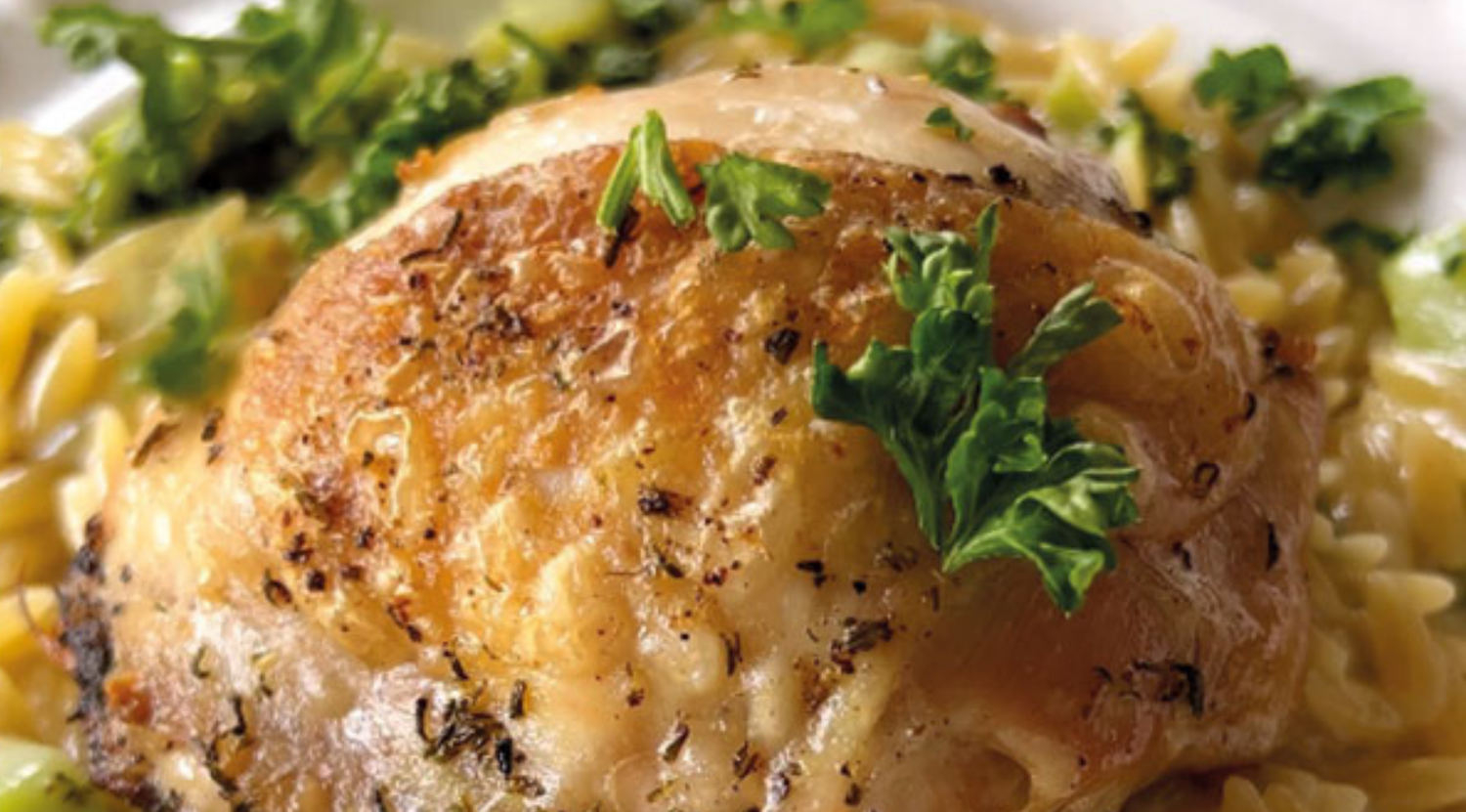 Ein perfekt gebratener Hähnchenschenkel mit Petersilie auf Kräuter-Orzo, elegant präsentiert auf einem weißen Teller - zubereitet im Fissler Kochgeschirr.