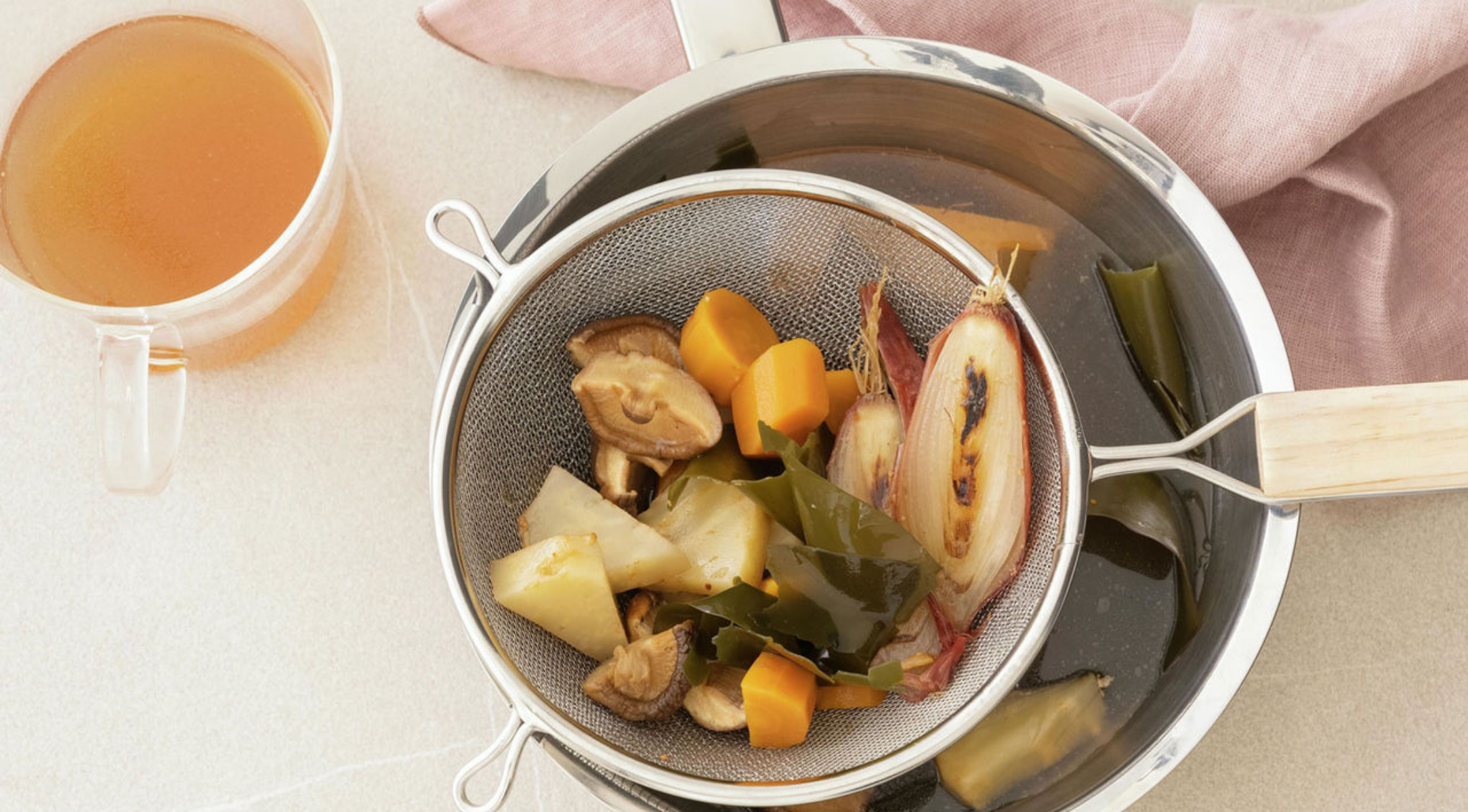 Das Fissler-Edelstahlsieb mit Gemüse ruht auf unserem charakteristischen Topf, die Brühe wird daneben serviert, alles auf einer glänzenden Oberfläche.