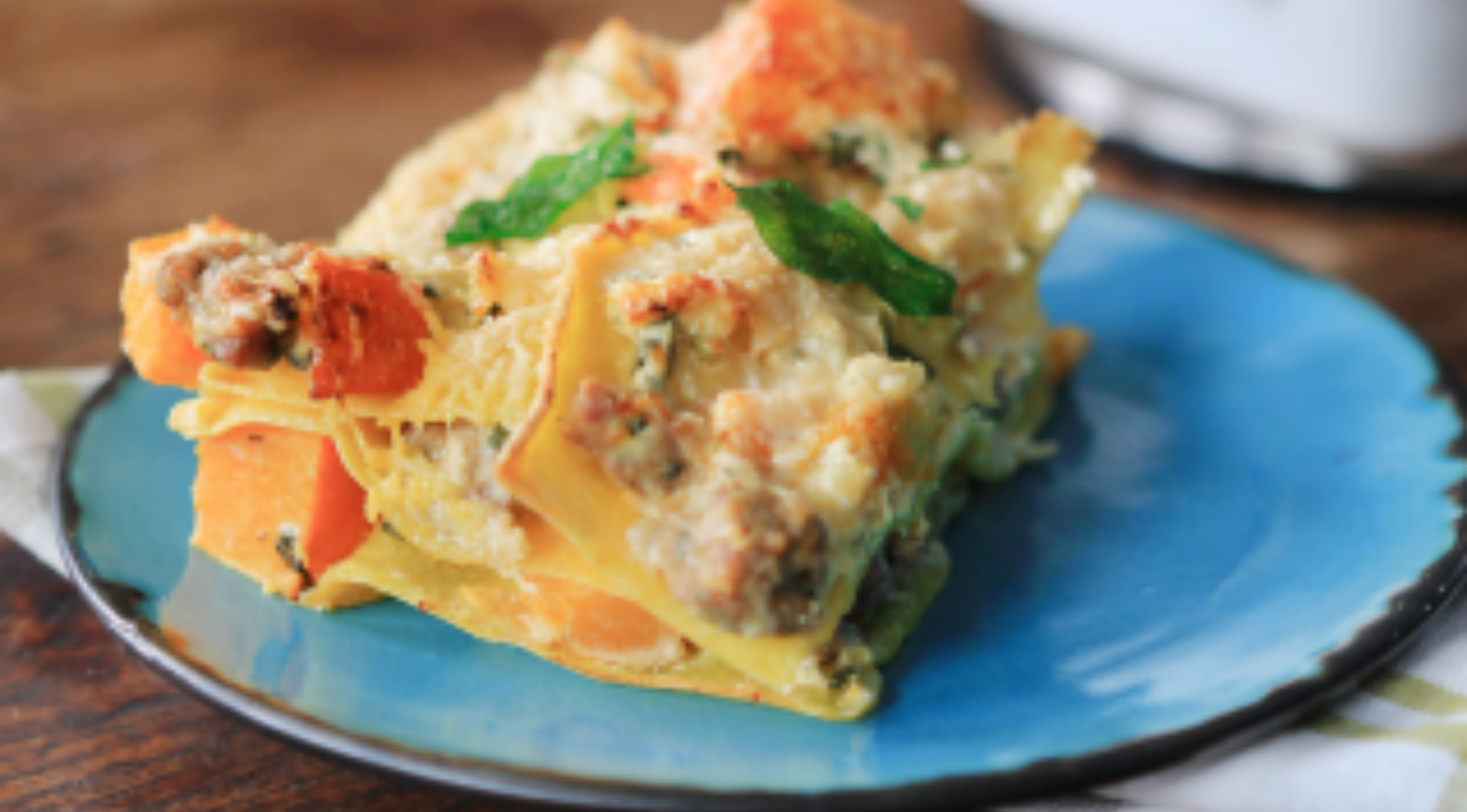 Ein Stück Lasagne mit Nudel-, Fleisch- und Käseschichten ruht auf einem blauen Teller - präsentiert mit Fissler-Präzision und zeitlosem Design.