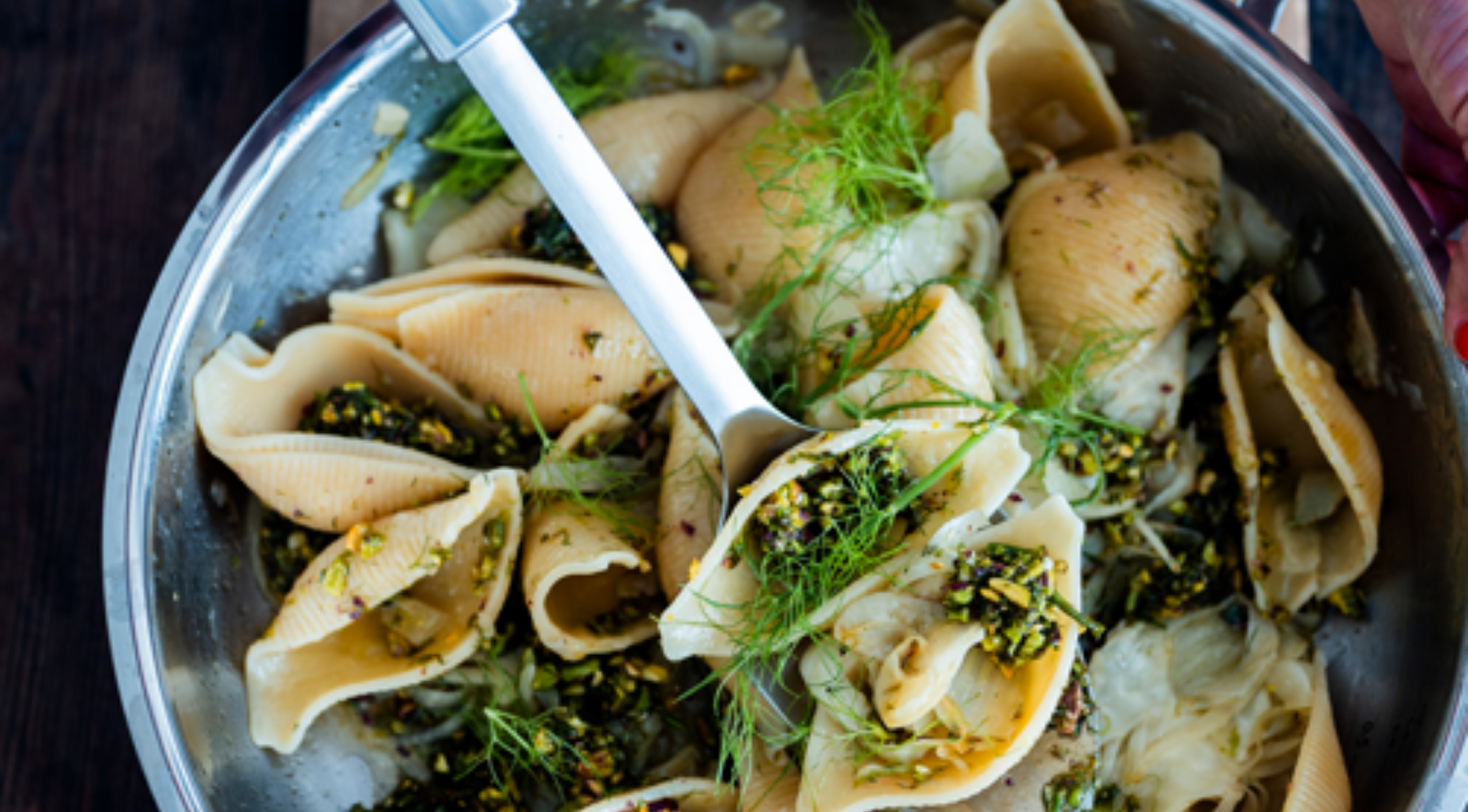 Fissler-Edelstahlpfanne mit gefüllten Nudelschalen, grüner Kräuterfüllung, frischer Dillgarnitur und Silberlöffel zum Servieren.