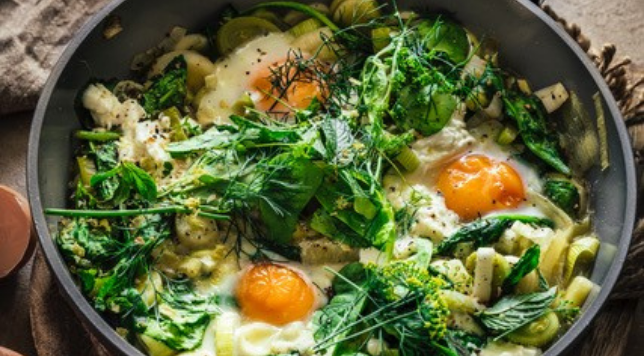 Eine Fissler-Pfanne mit perfekt gegarten Eiern, Blattgemüse und Gemüse, elegant garniert, ist ein Musterbeispiel für deutsches Präzisionskochgeschirr.